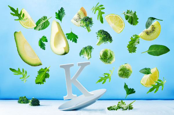 Letra K em cima de prato; ao redor, frutas e verduras flutuando, em fundo azul e superfície branca