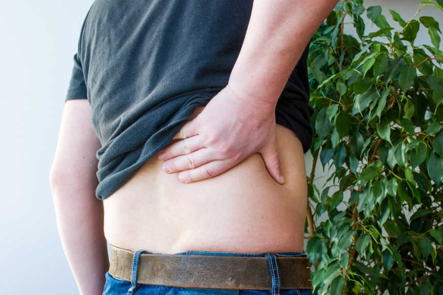 Homem com a mÃ£o sobre as costas, em sinal de dor lombar, um sintoma da pielonefrite.