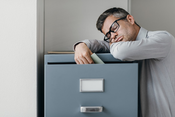 Homem dormindo apoiado em um armário de arquivos, uma alusão à narcolepsia.